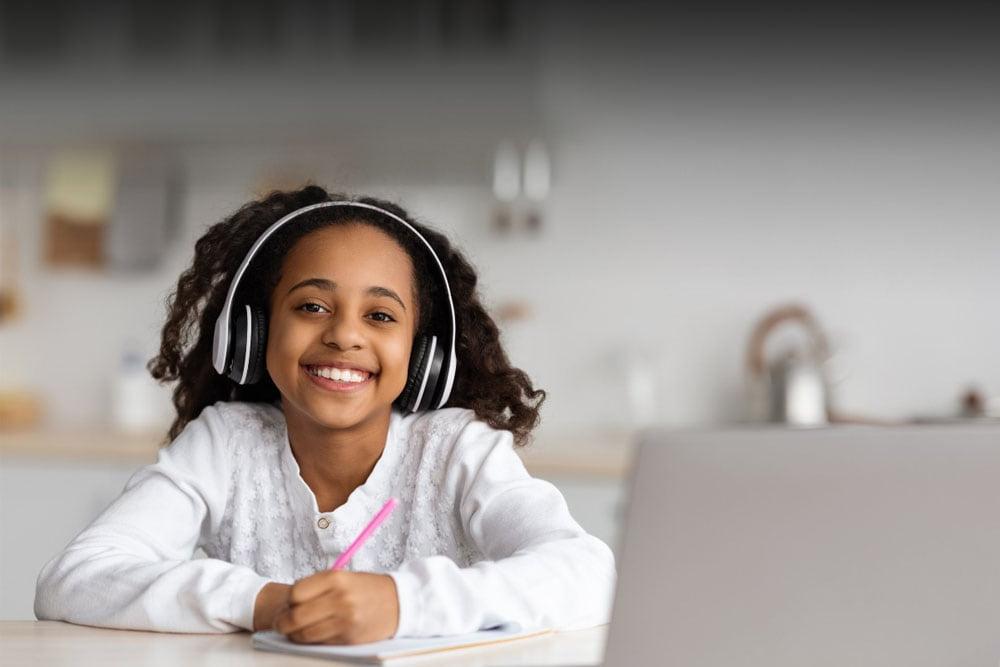 Coastal Connections Academy student in a white shirt taking an online class smiling at the camera.